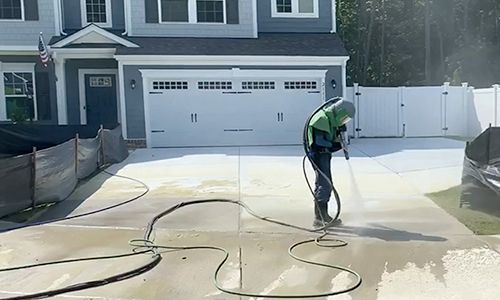 A man is using a pressure washer to clean a driveway in front of a house.