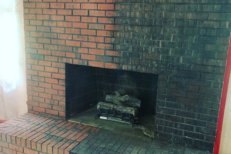 A brick fireplace with logs in it in a living room.