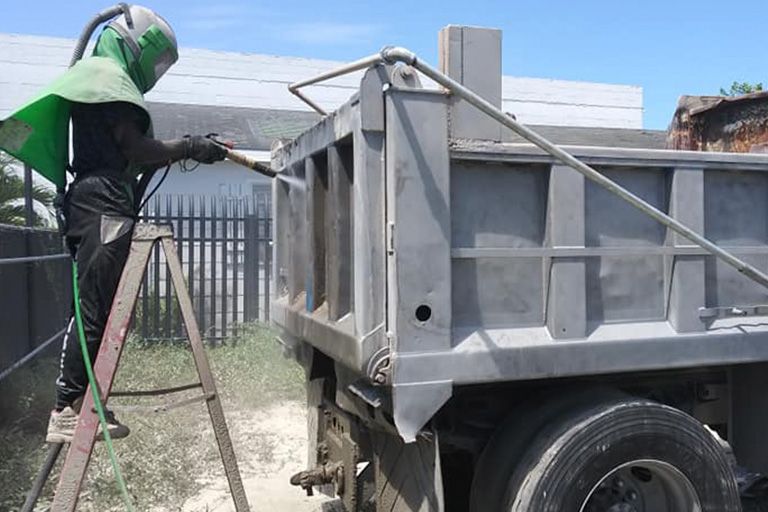 A man is sandblasting the side of a dump truck.