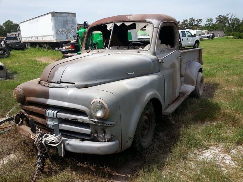 An old truck with a broken windshield is parked in a grassy field