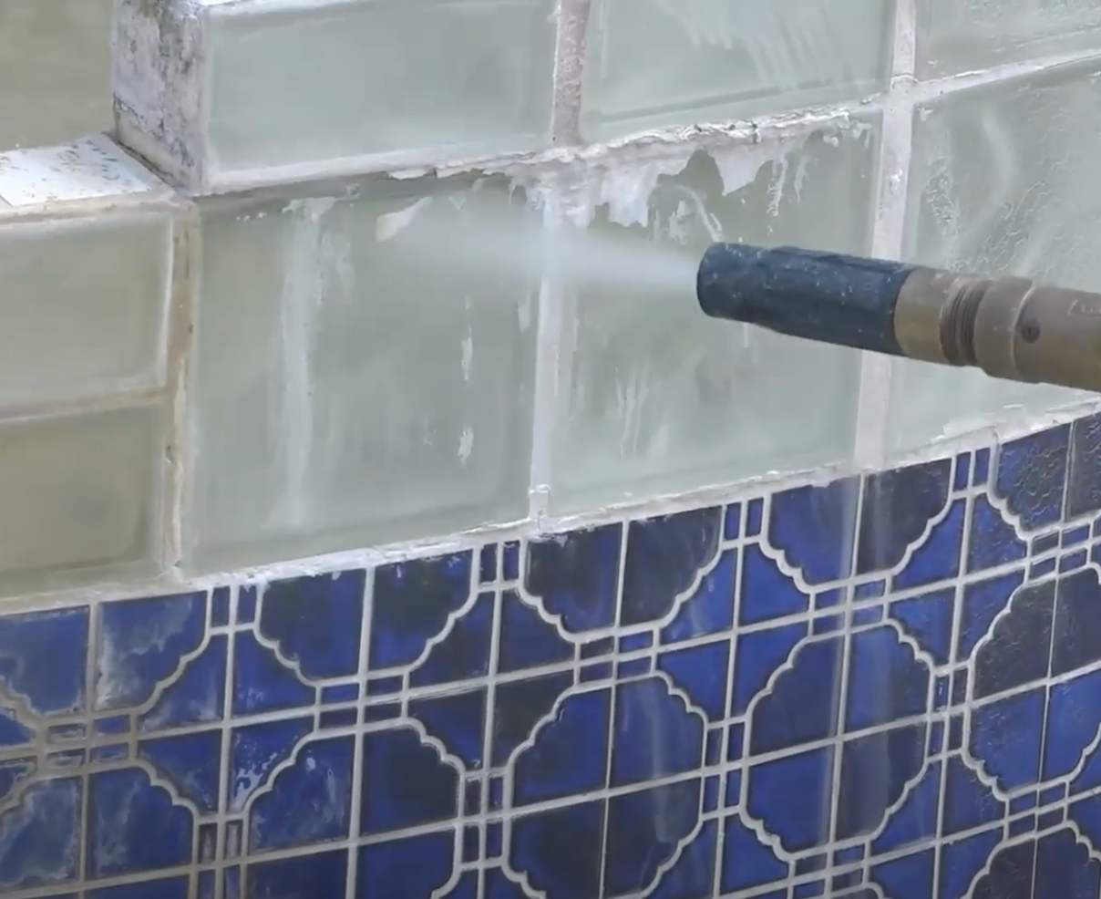 A person is cleaning a tile wall with a high pressure washer.