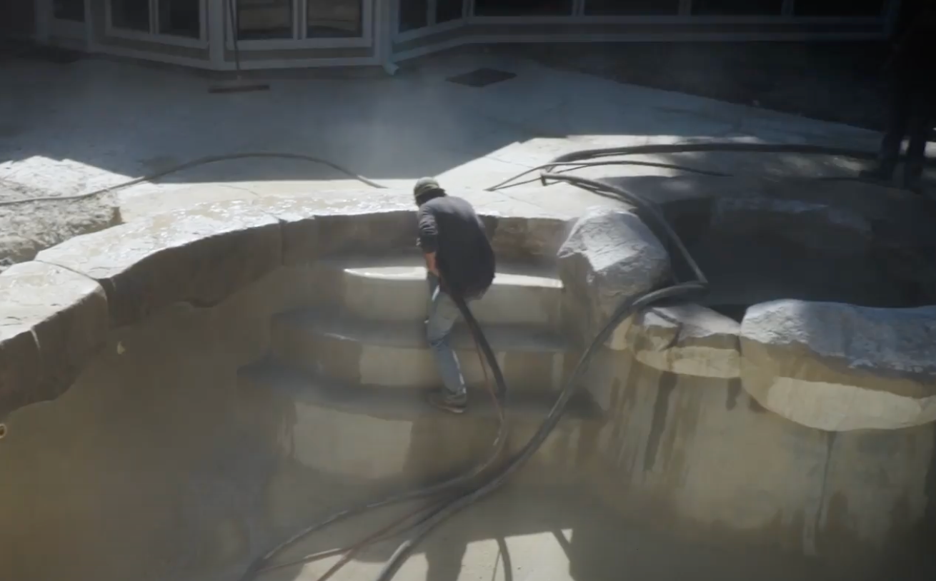 A man is cleaning the steps of a pool with a hose.