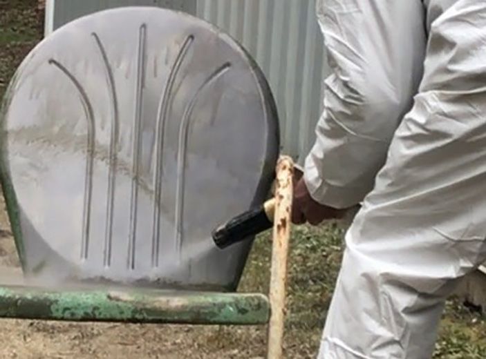 A man in a white suit is holding a hammer next to a chair.