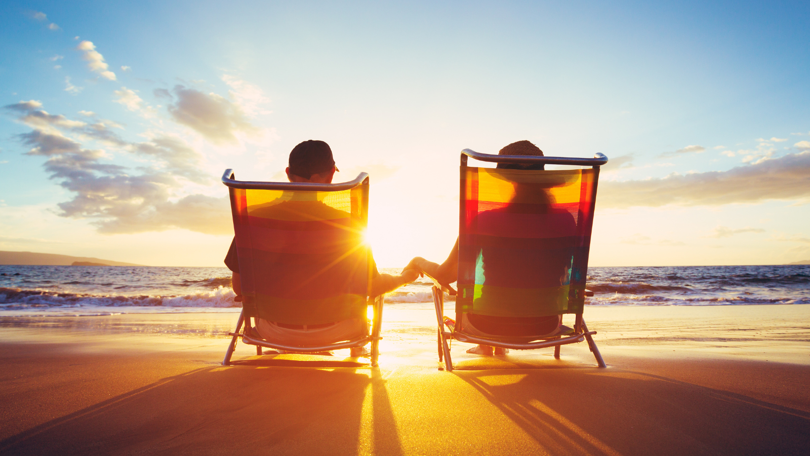 A man and a woman are sitting in beach chairs on the beach holding hands.