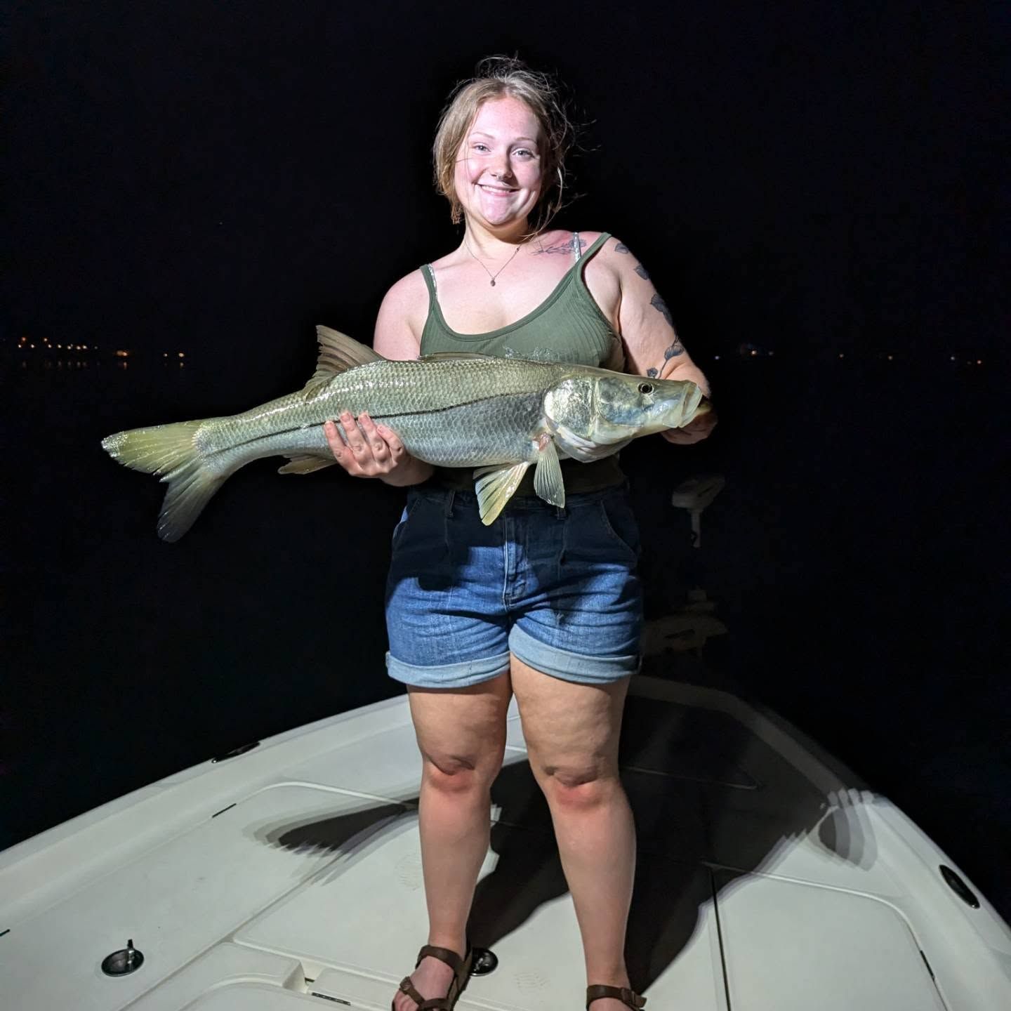 A woman is standing on a boat holding a large fish.