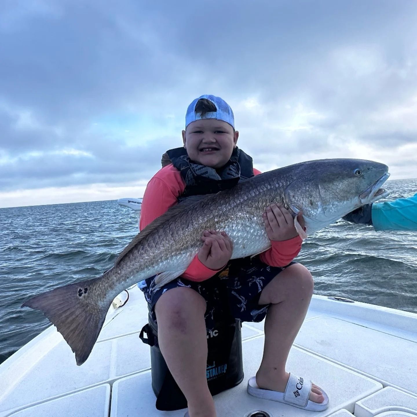 A young boy is sitting on a boat holding a large fish.
