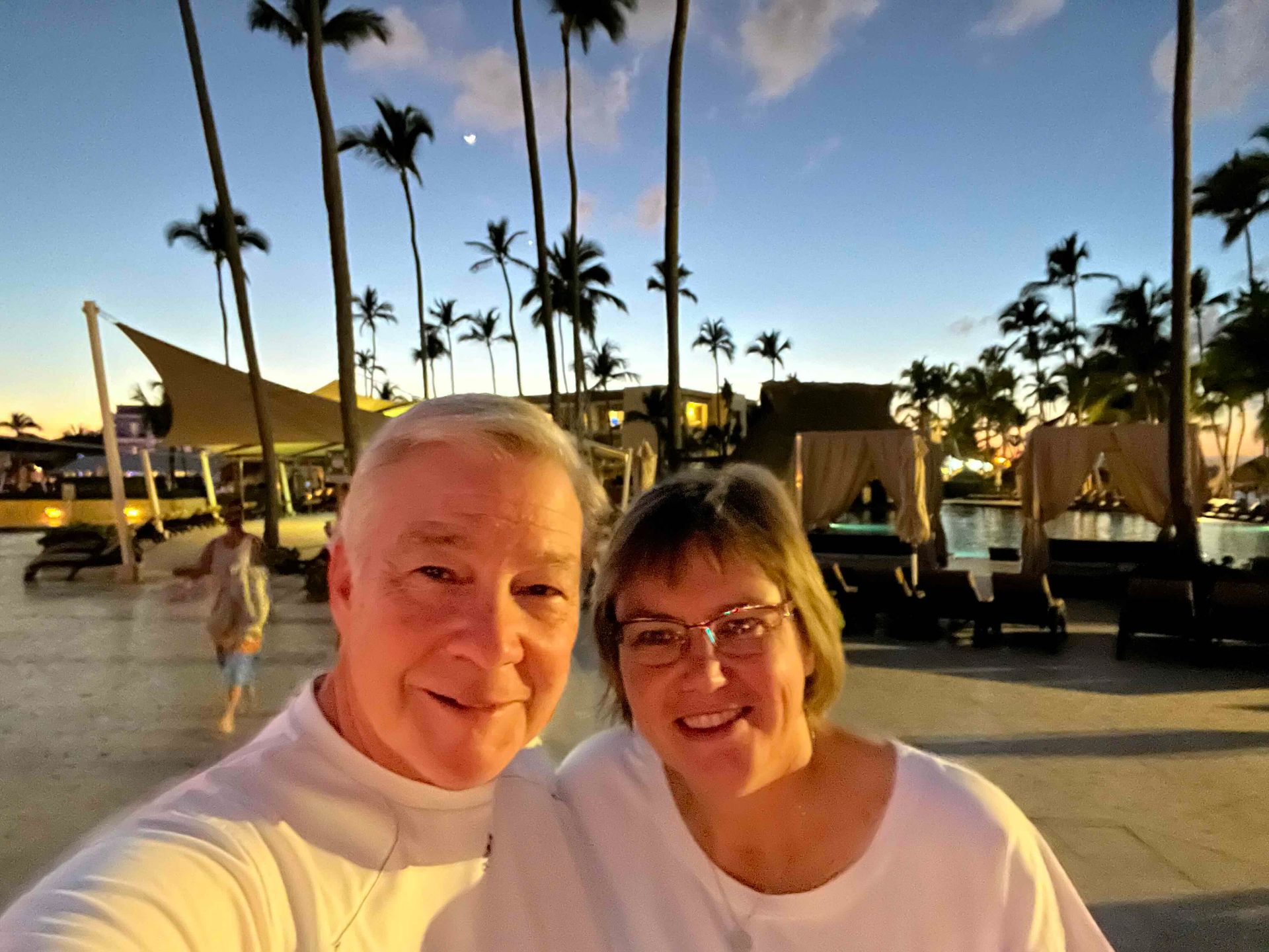 A man and a woman are posing for a selfie in front of palm trees.