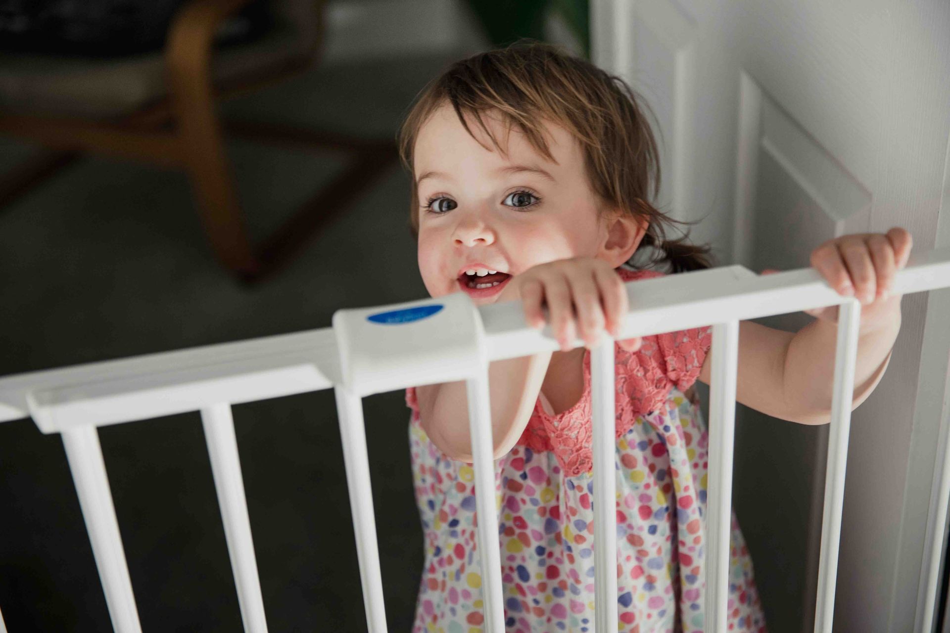 A little girl is standing behind a baby gate.