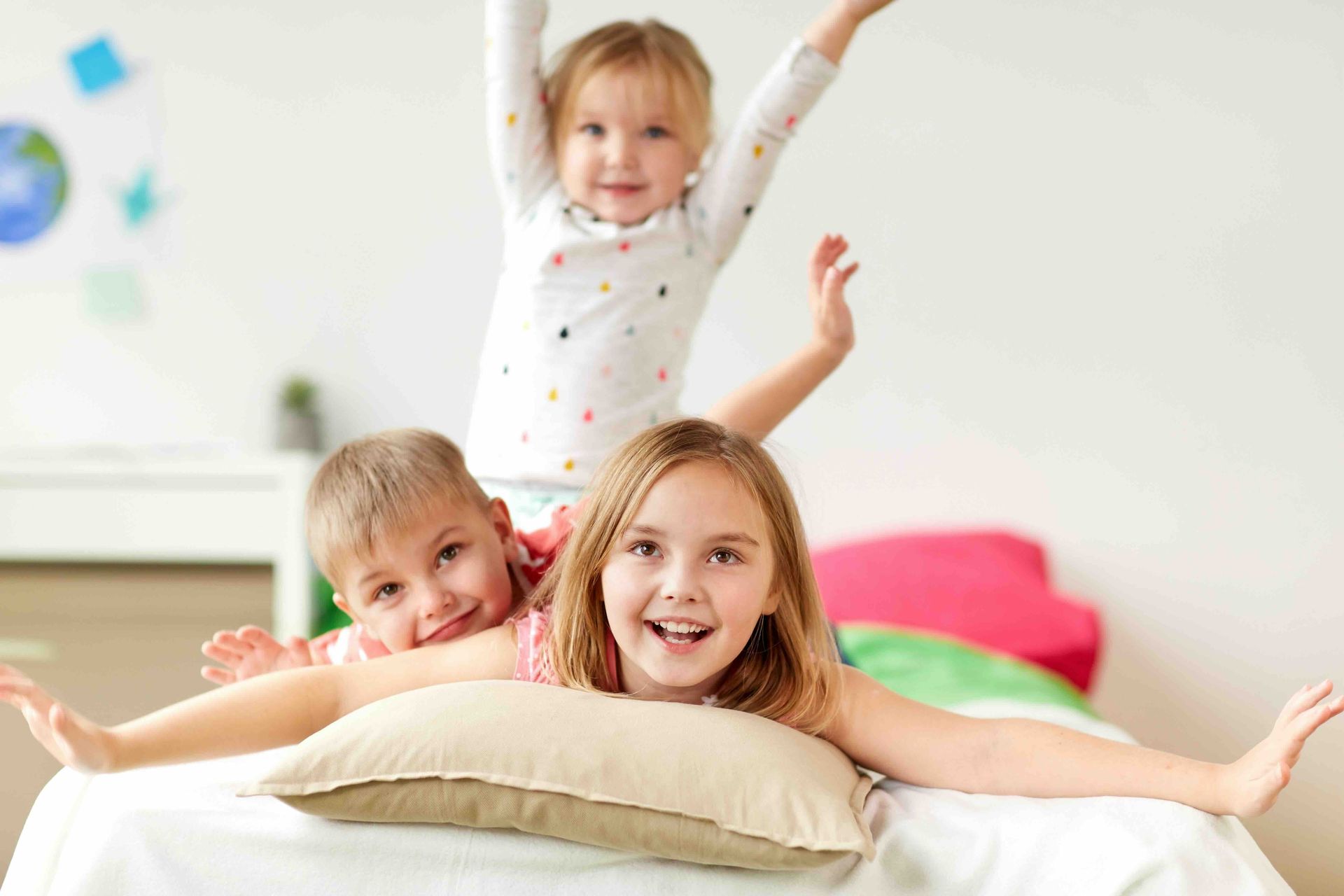 Three children are playing on a bed with a pillow.