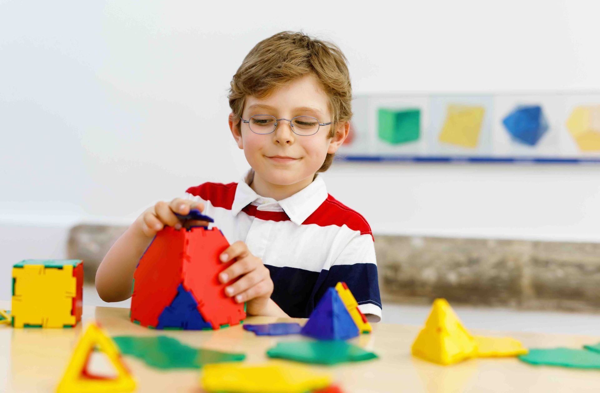 A young boy is sitting at a table playing with geometric shapes.