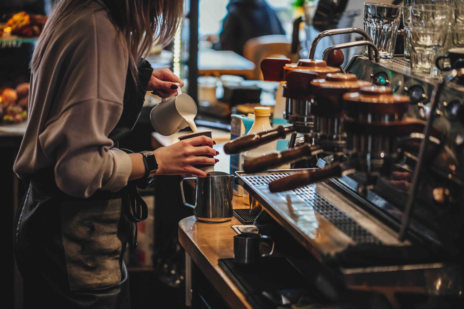 A woman is making a cup of coffee in a coffee shop.