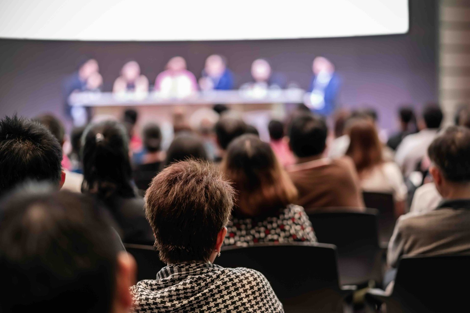 Audience watching a panel discussion on a stage; blurred background.