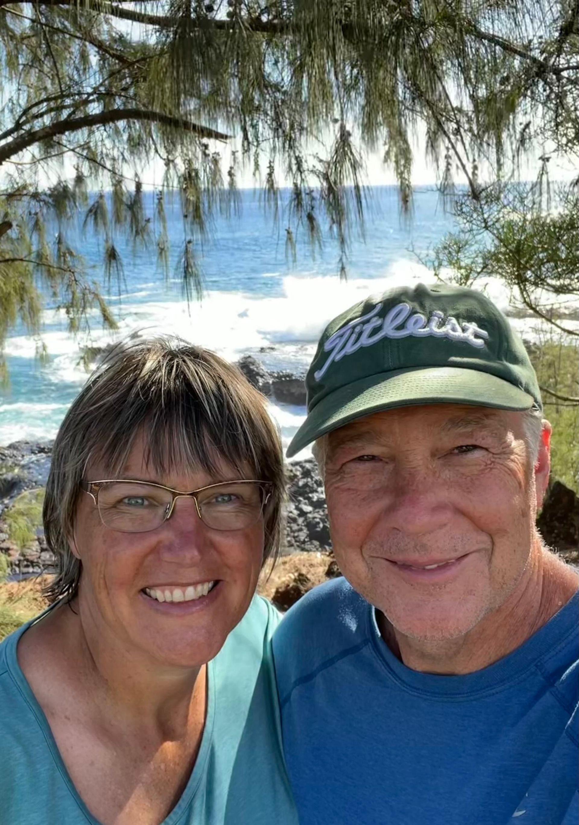 A man and a woman are posing for a picture in front of the ocean.