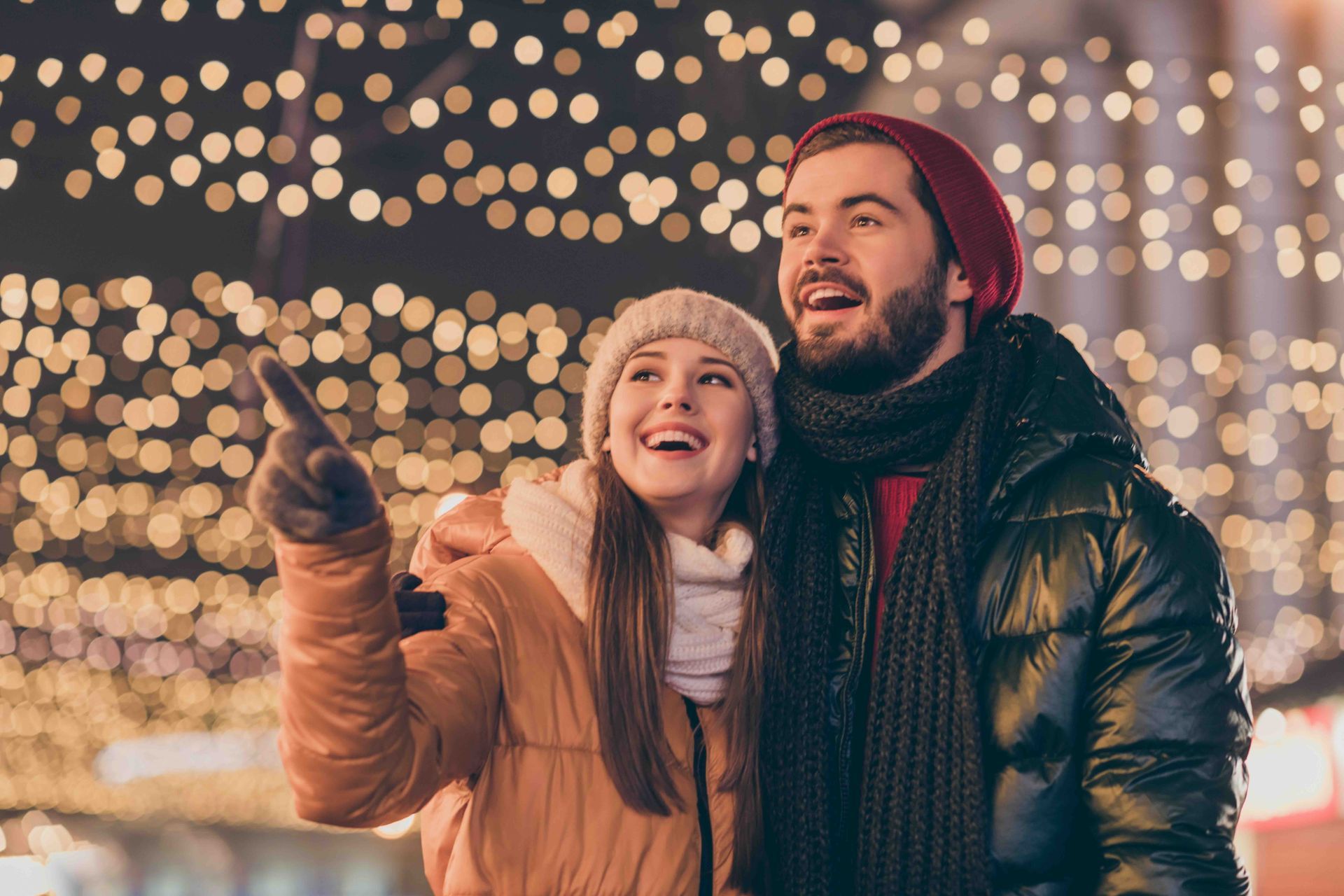 A man and a woman are standing next to each other in front of Christmas lights.