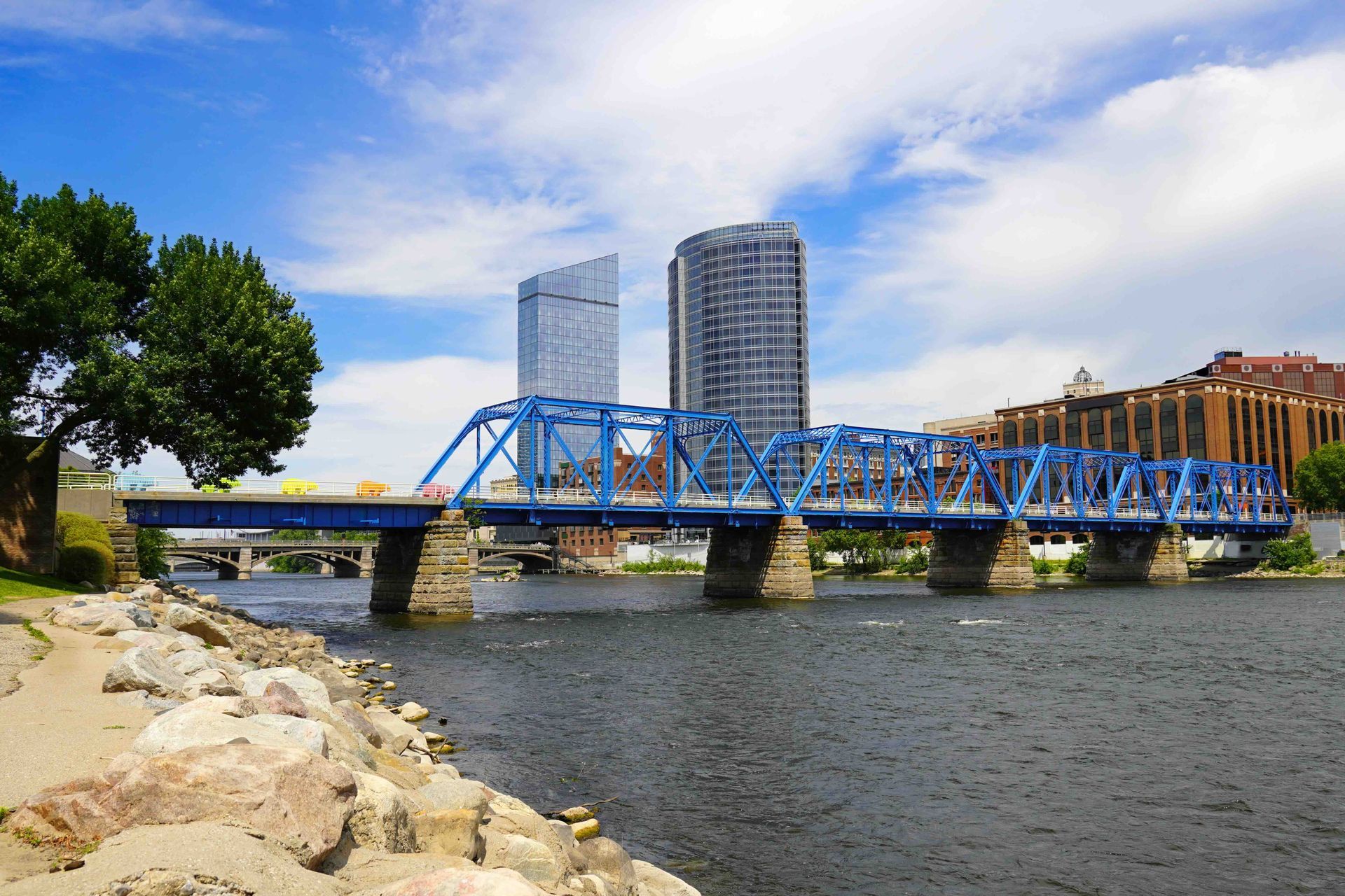 A blue bridge over a river with a city in the background