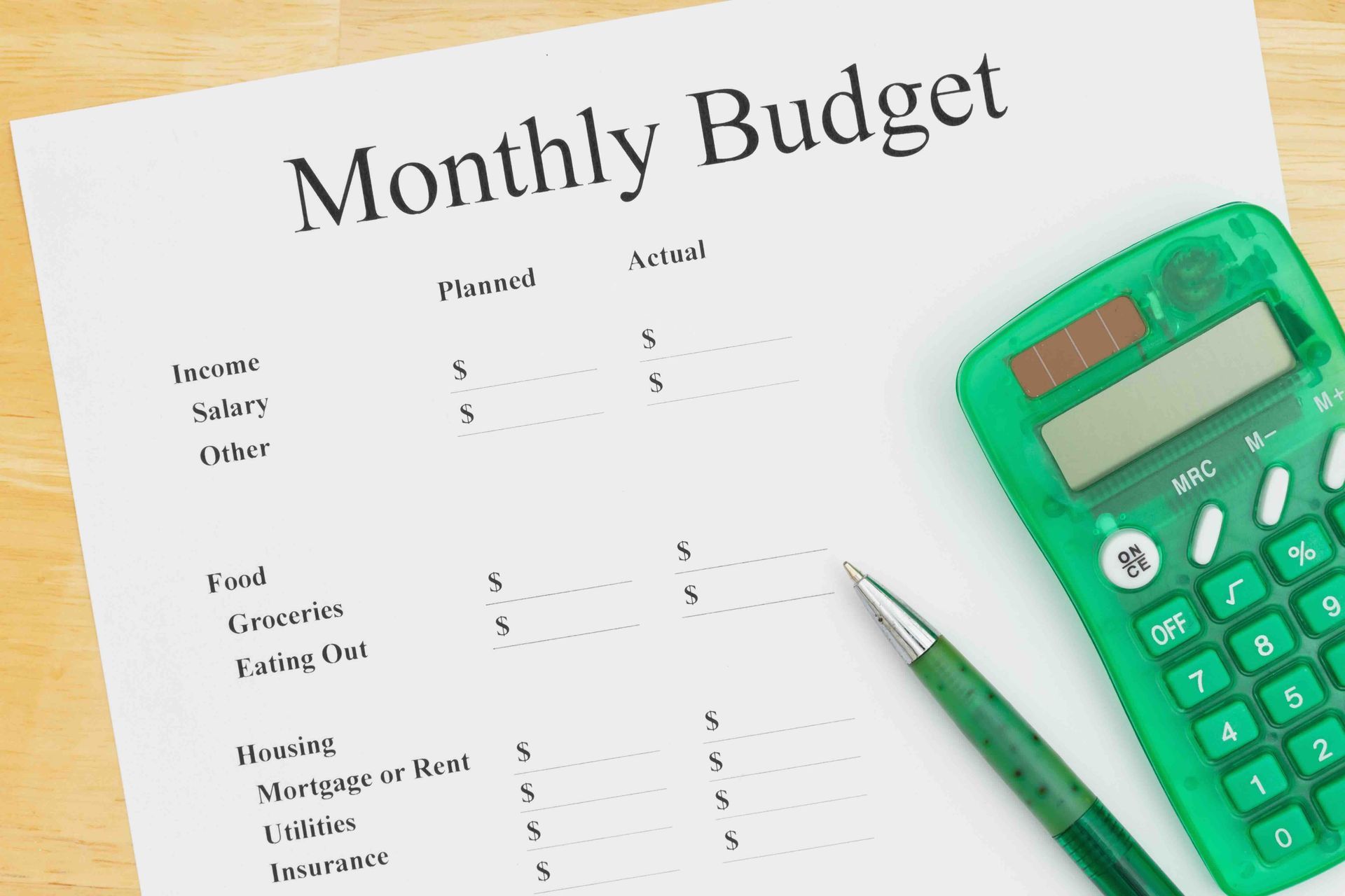 Monthly budget document with a pen and green calculator on a wooden surface.