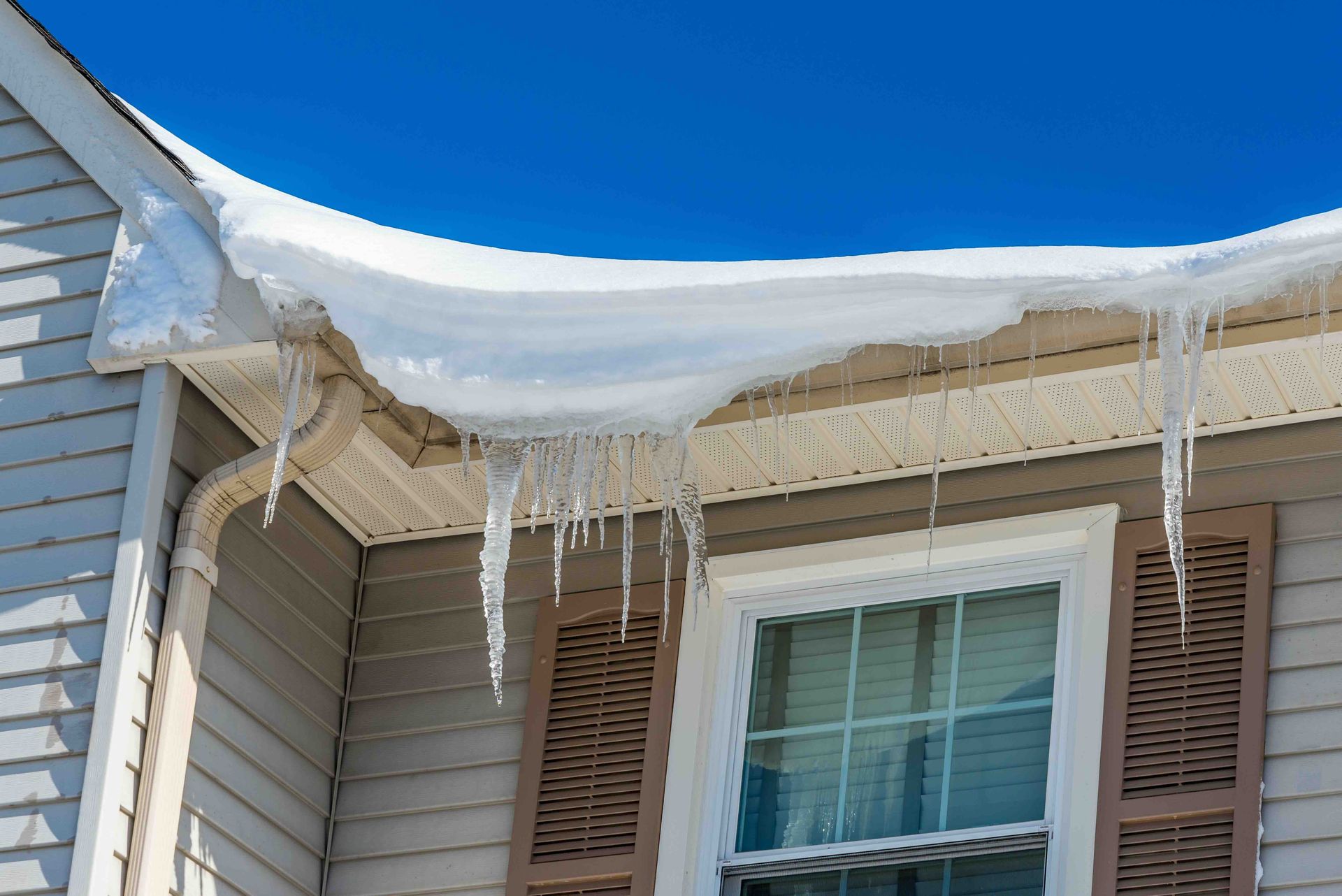 Snow and icicles on the roof of a house with a blue sky background.