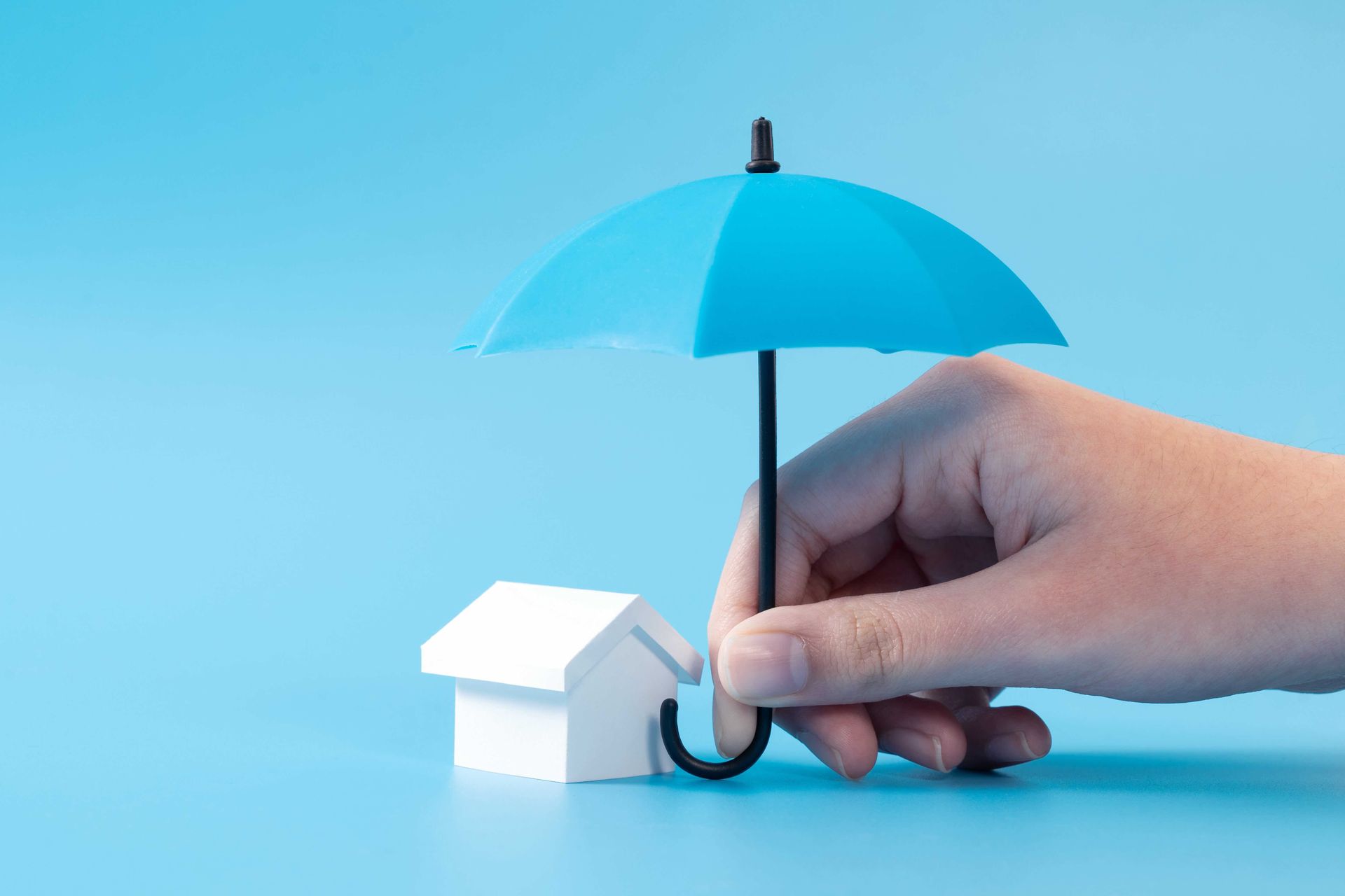 A hand is holding a blue umbrella over a small white house.