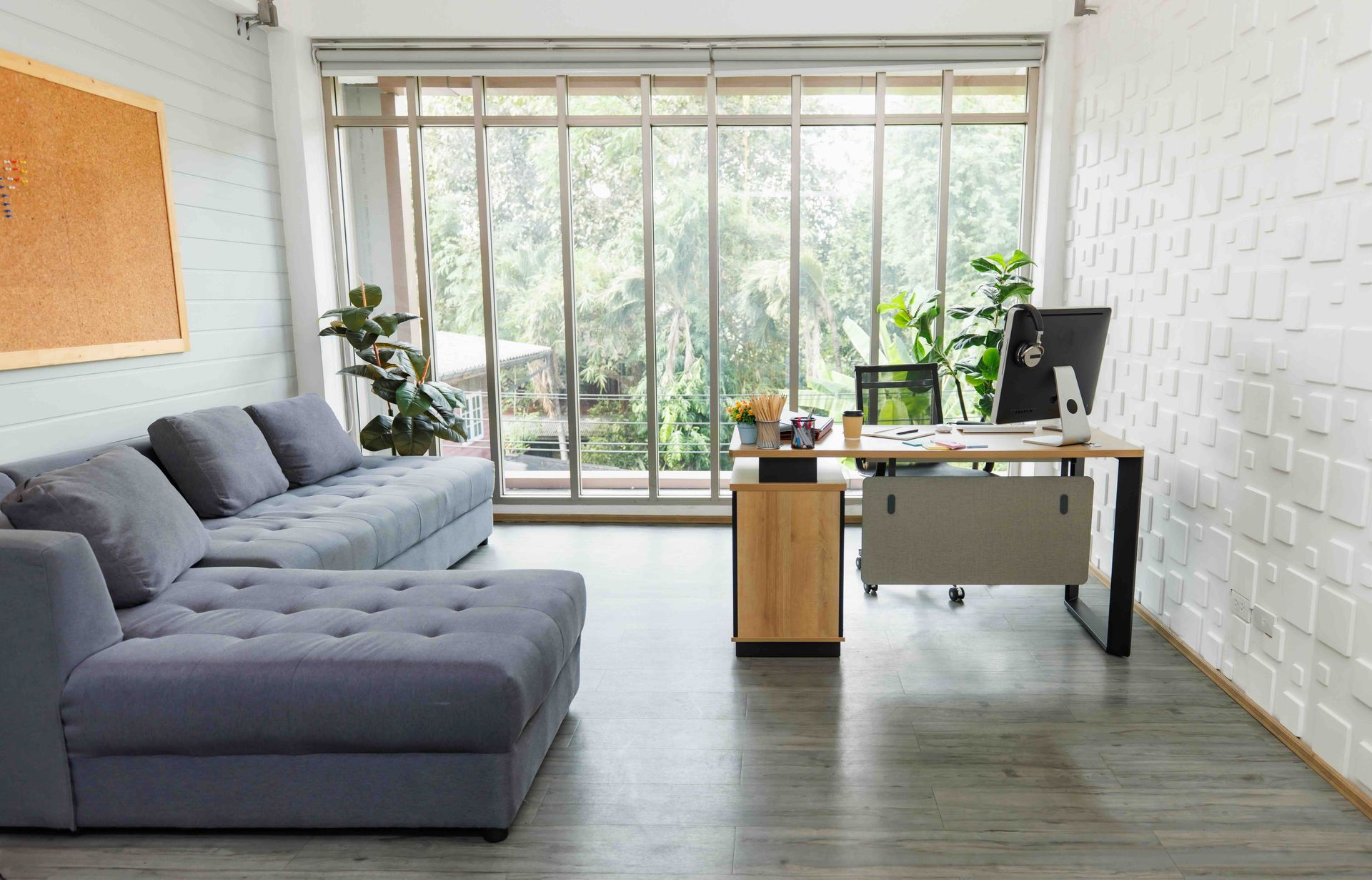 A home office with a couch, desk, and large windows.