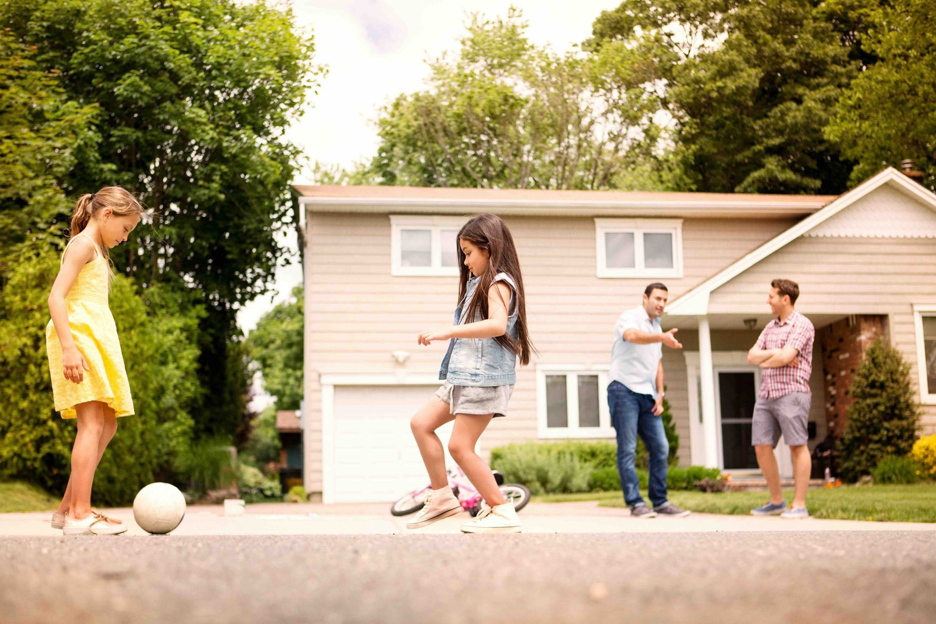 A family is playing soccer on the sidewalk in front of their house.