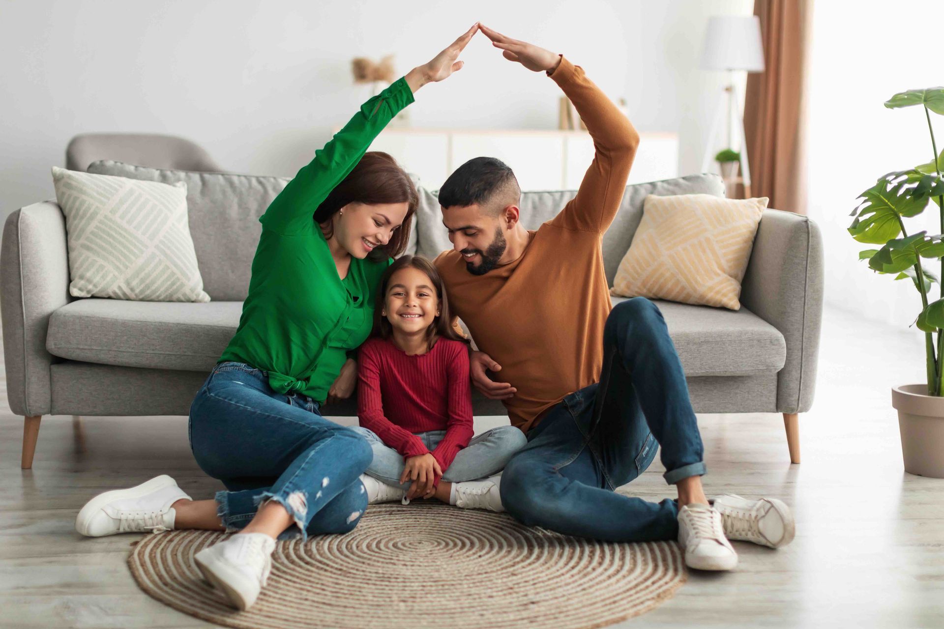 A family is sitting on the floor in a living room making a house with their hands.