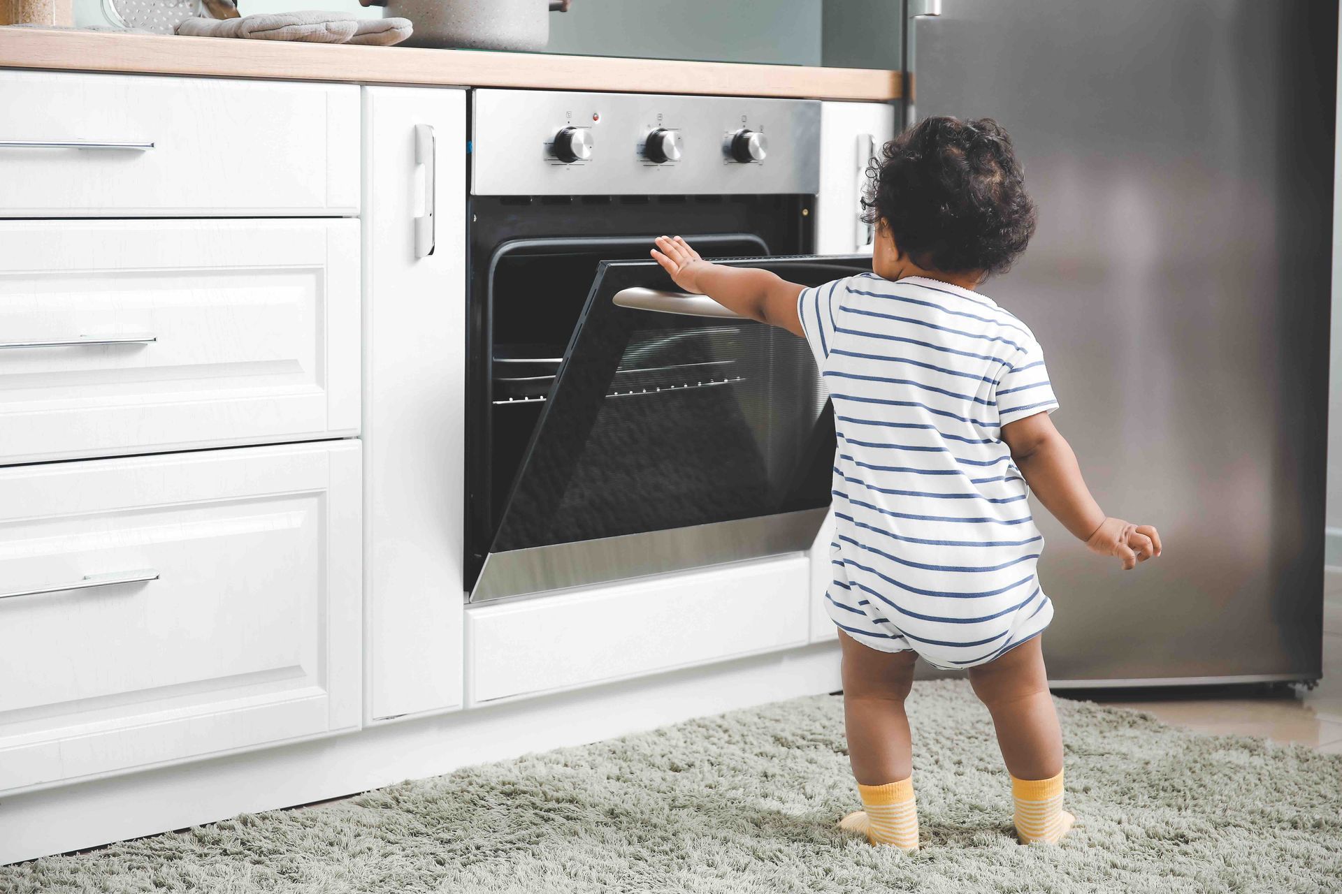 A baby is standing in front of an oven in a kitchen.