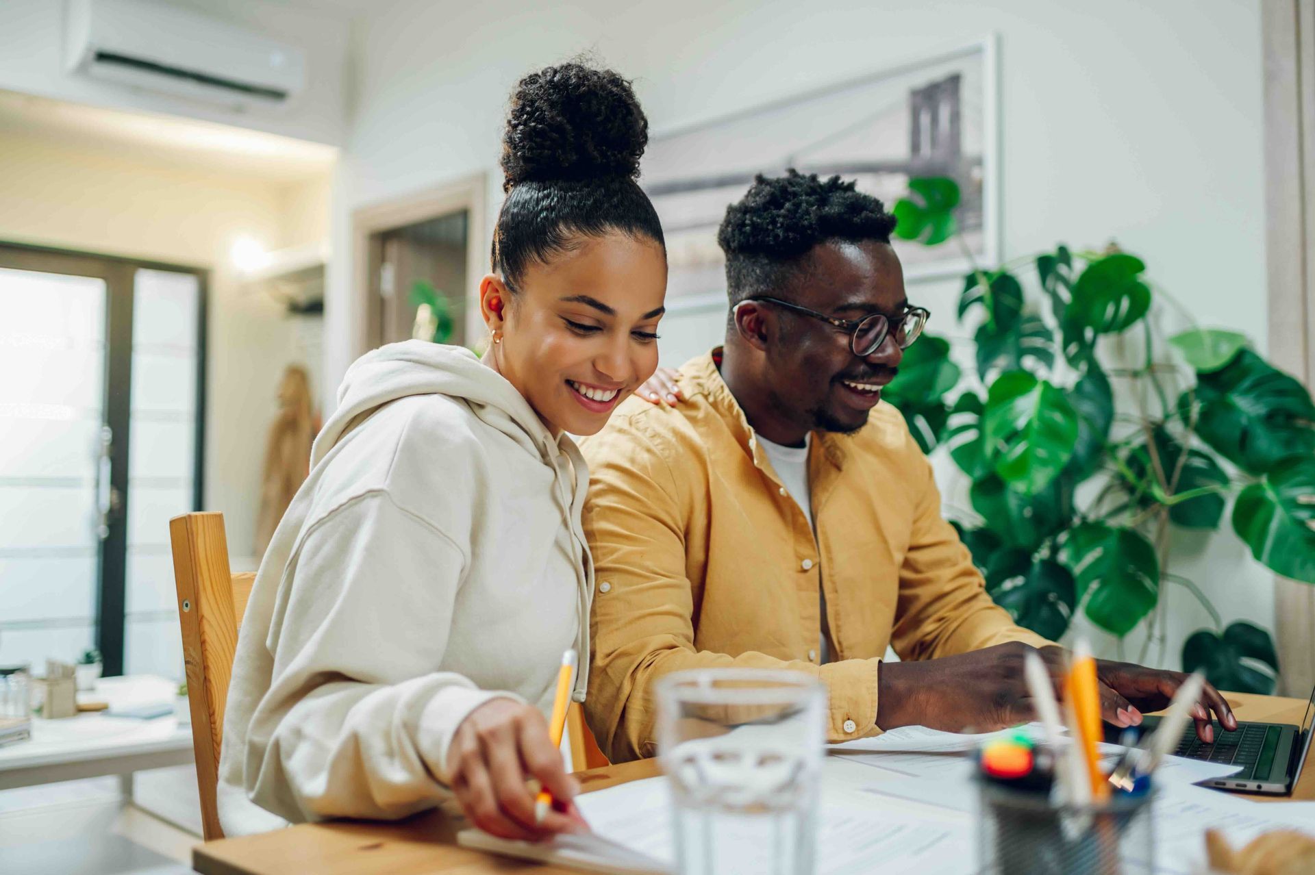 A man and a woman are sitting at a table looking at a laptop.