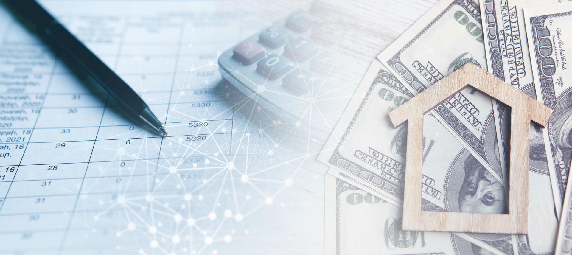 A wooden house cutout is sitting on top of a pile of money next to a pen and calculator.