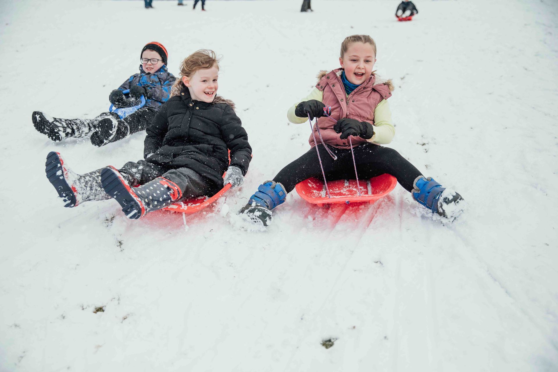 Three children are sledding down a snow-covered hill.