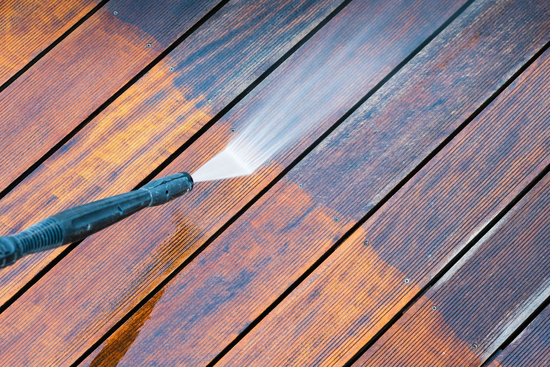 A person is using a high pressure washer to clean a wooden deck.