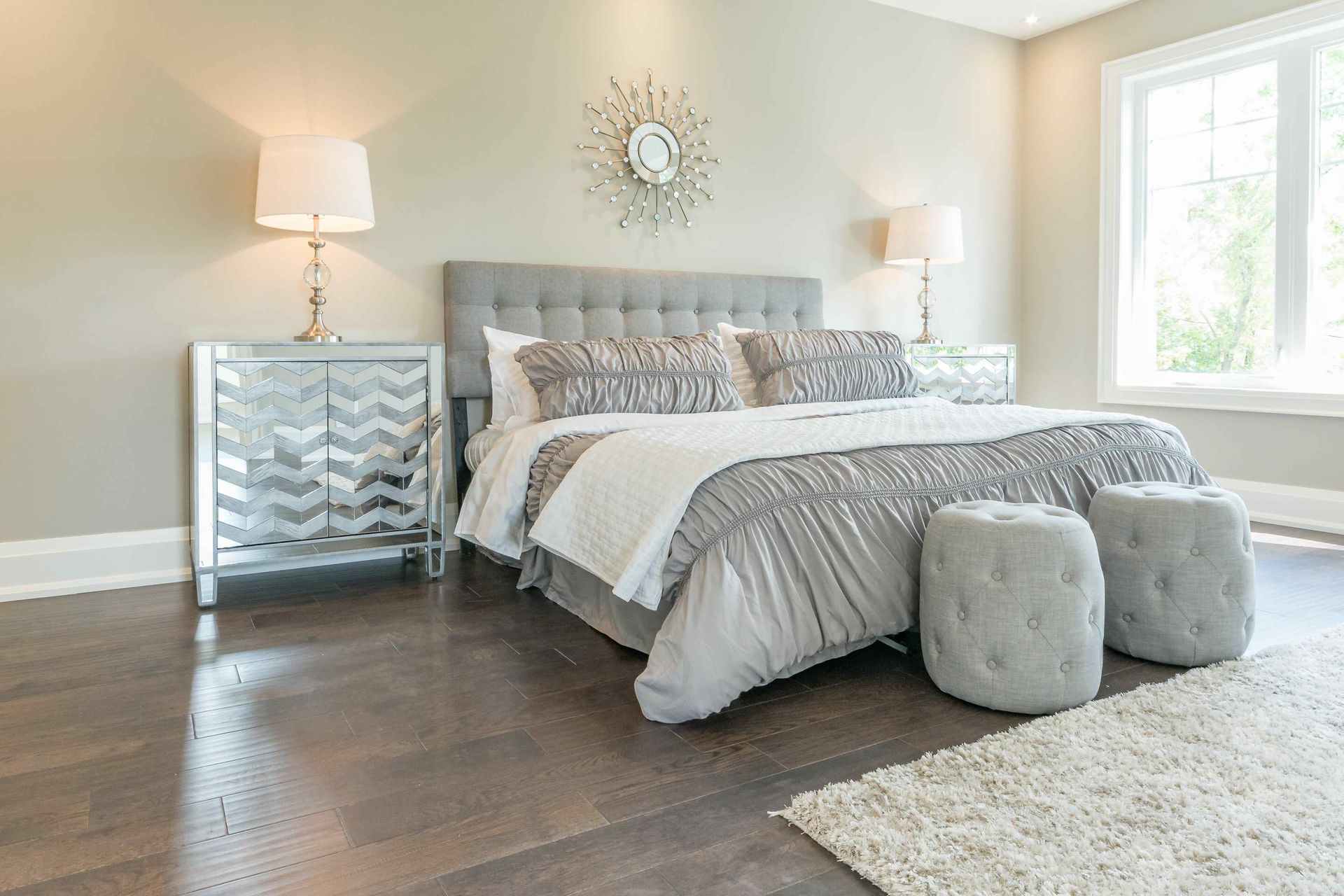 A bedroom with a king size bed , two ottomans , two lamps and a mirror on the wall.