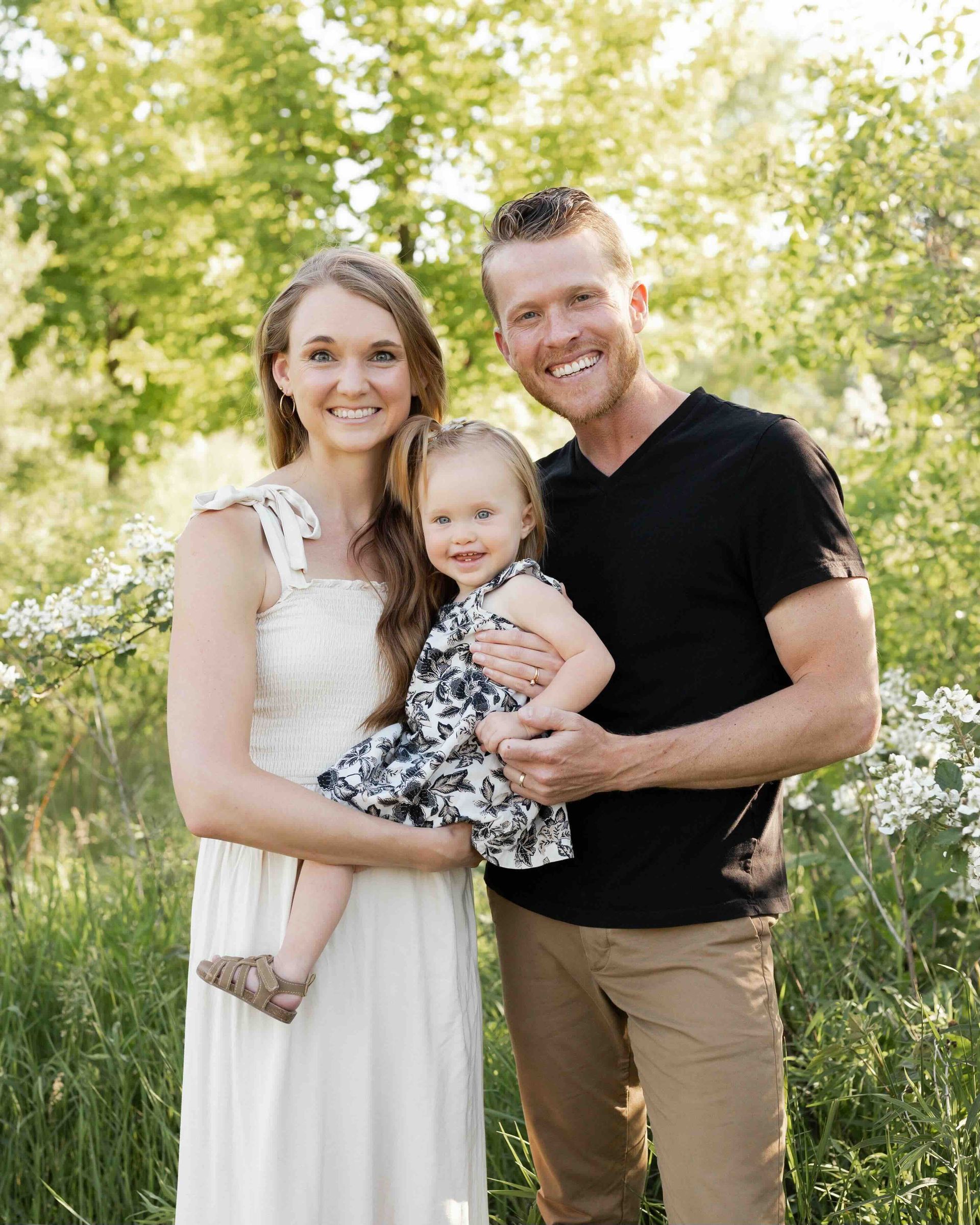 A man and woman are holding a little girl in a field.