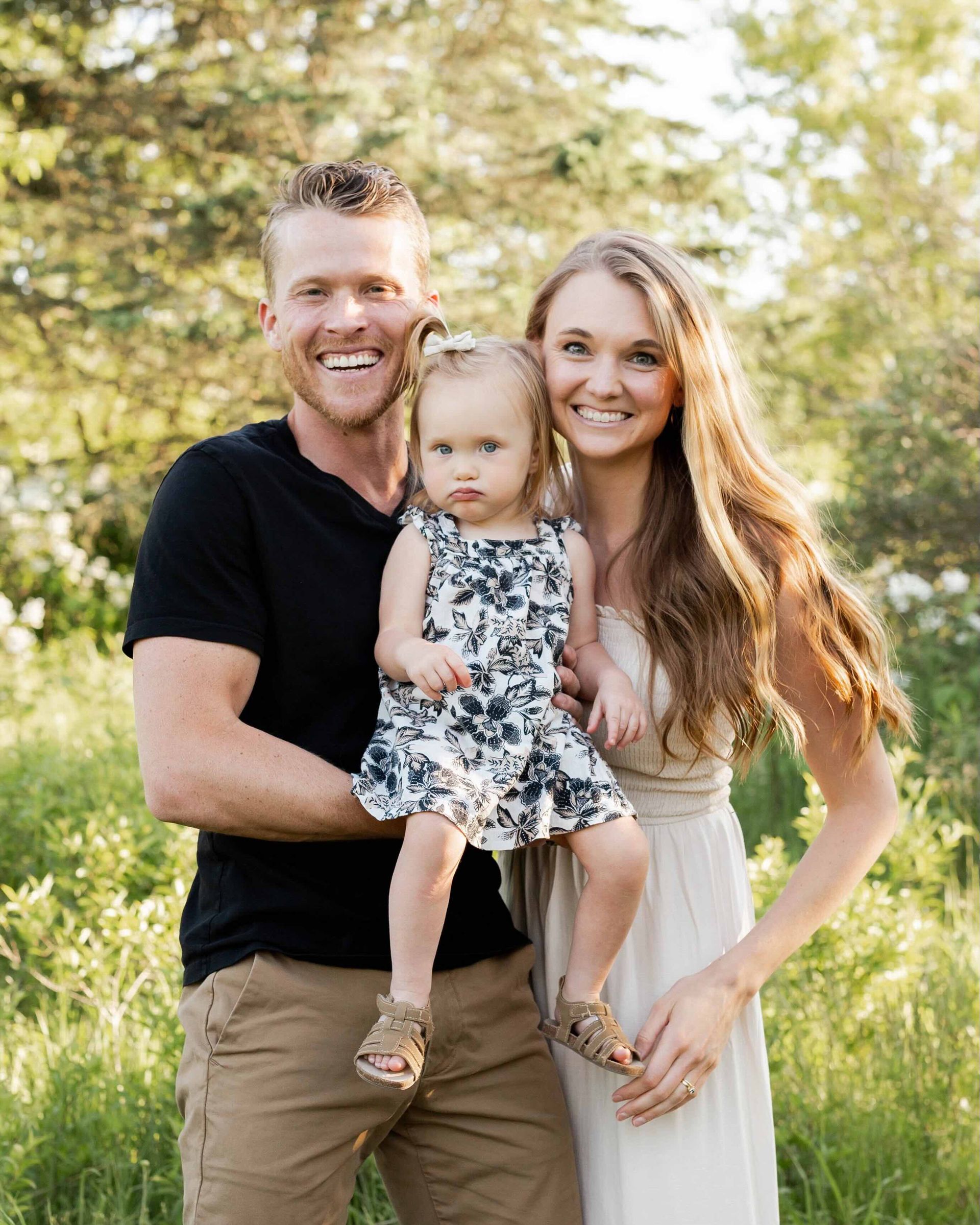A man and woman are holding a baby girl in a field.