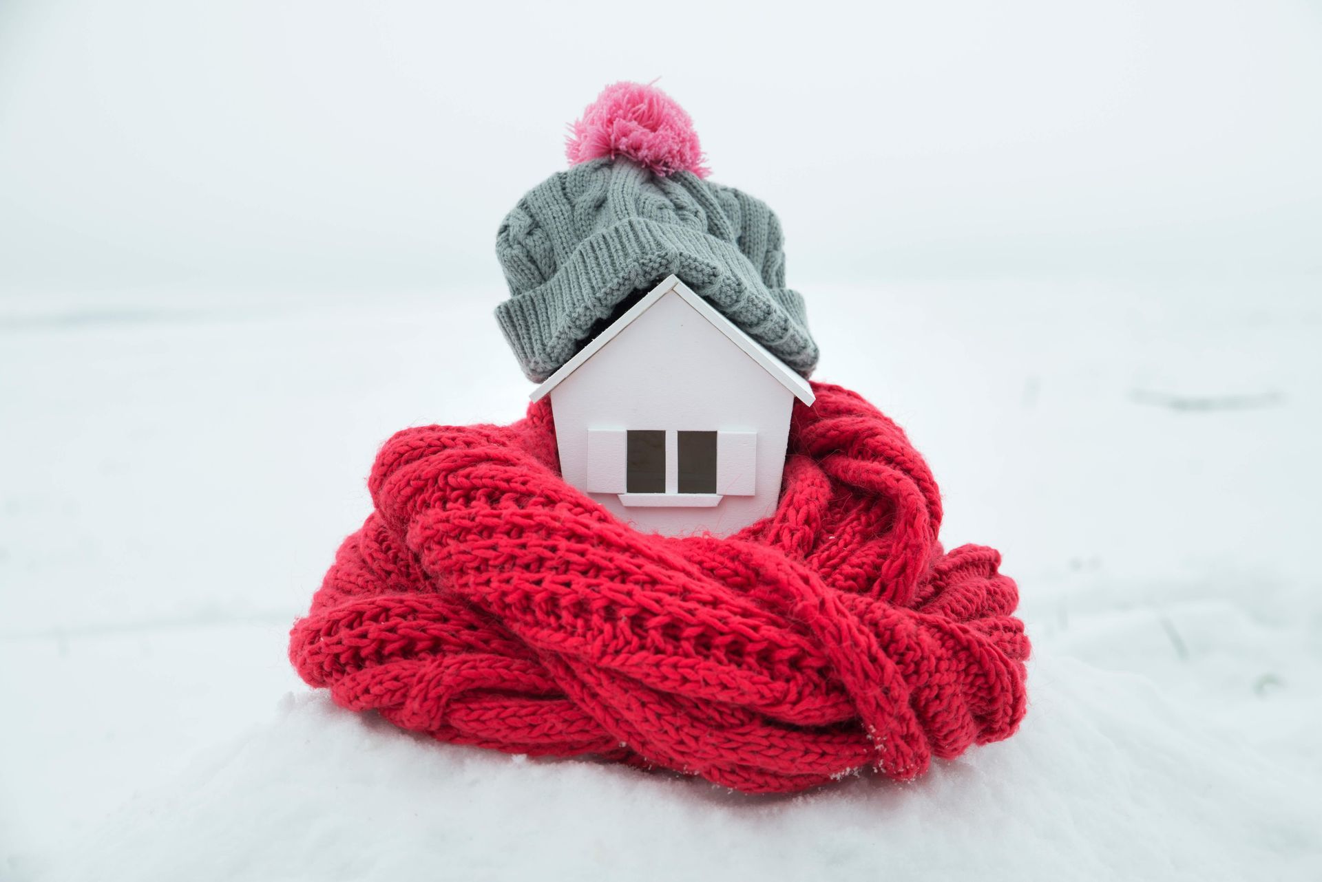 A small house wrapped in a scarf and hat in the snow.