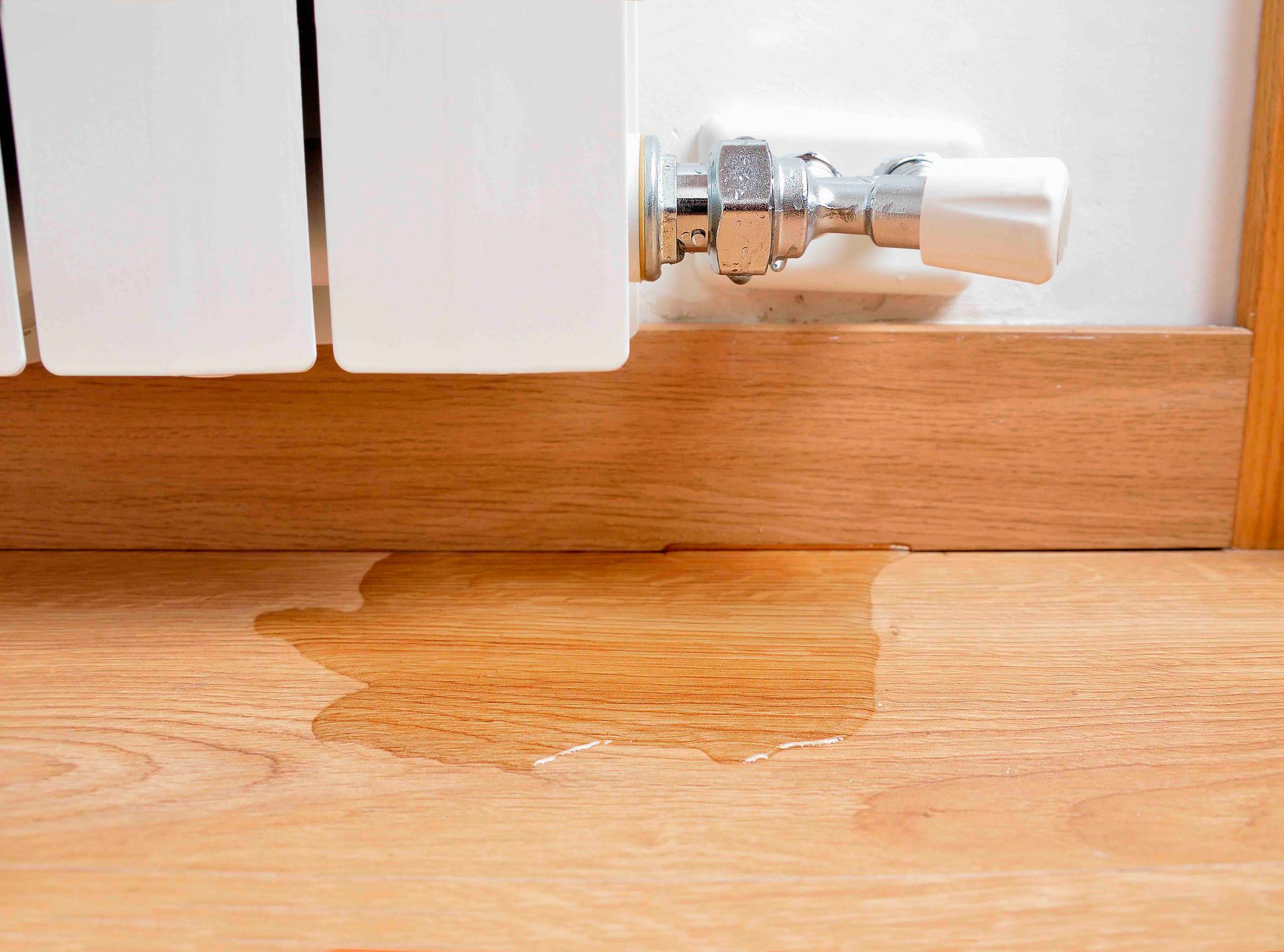 A radiator is leaking water on a wooden floor.