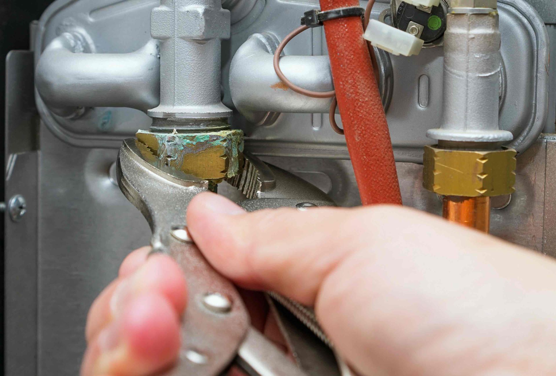 A person is fixing a boiler with a wrench.