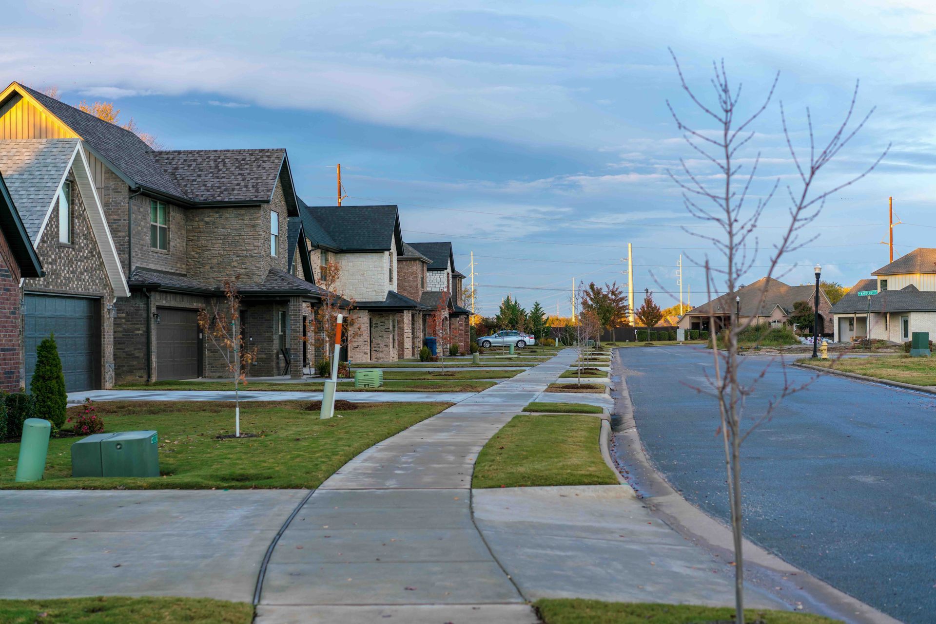 Row of new brick homes along a sidewalk on a suburban street under a cloudy sky.