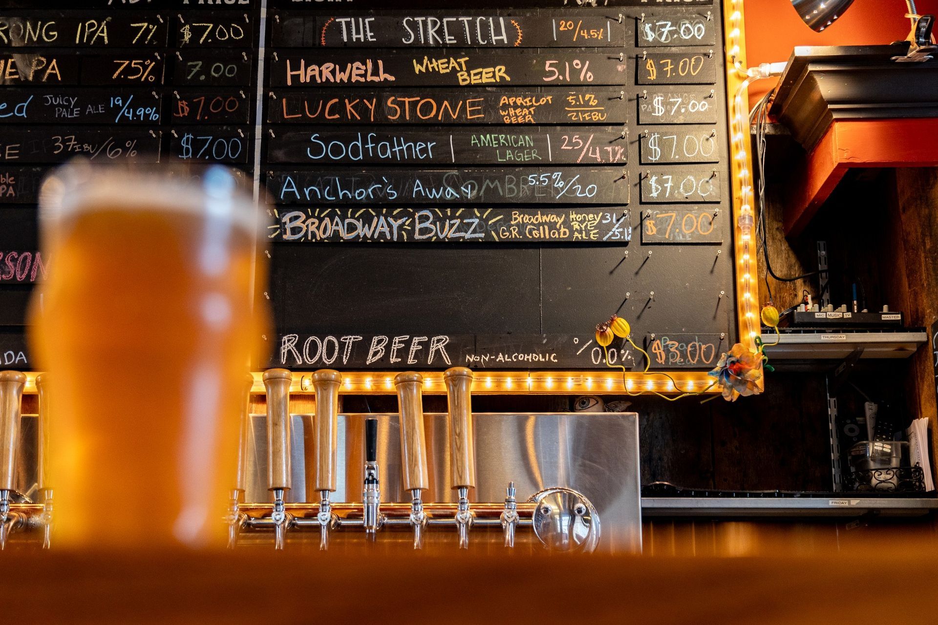 A glass of beer is sitting in front of a chalkboard with a list of beers on it.