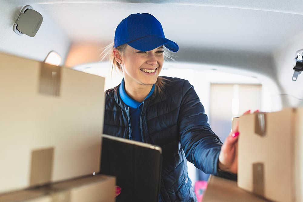 A delivery woman is carrying boxes in the back of a van.