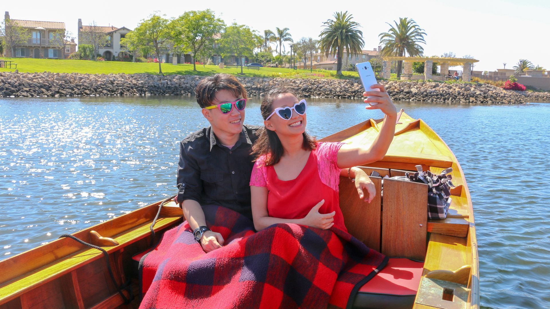 A man and a woman are sitting in a boat taking a selfie.