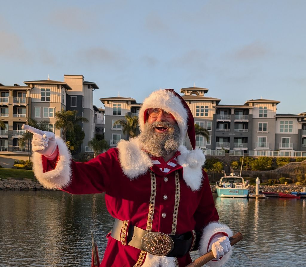 A man dressed as santa claus is pointing at something in the water