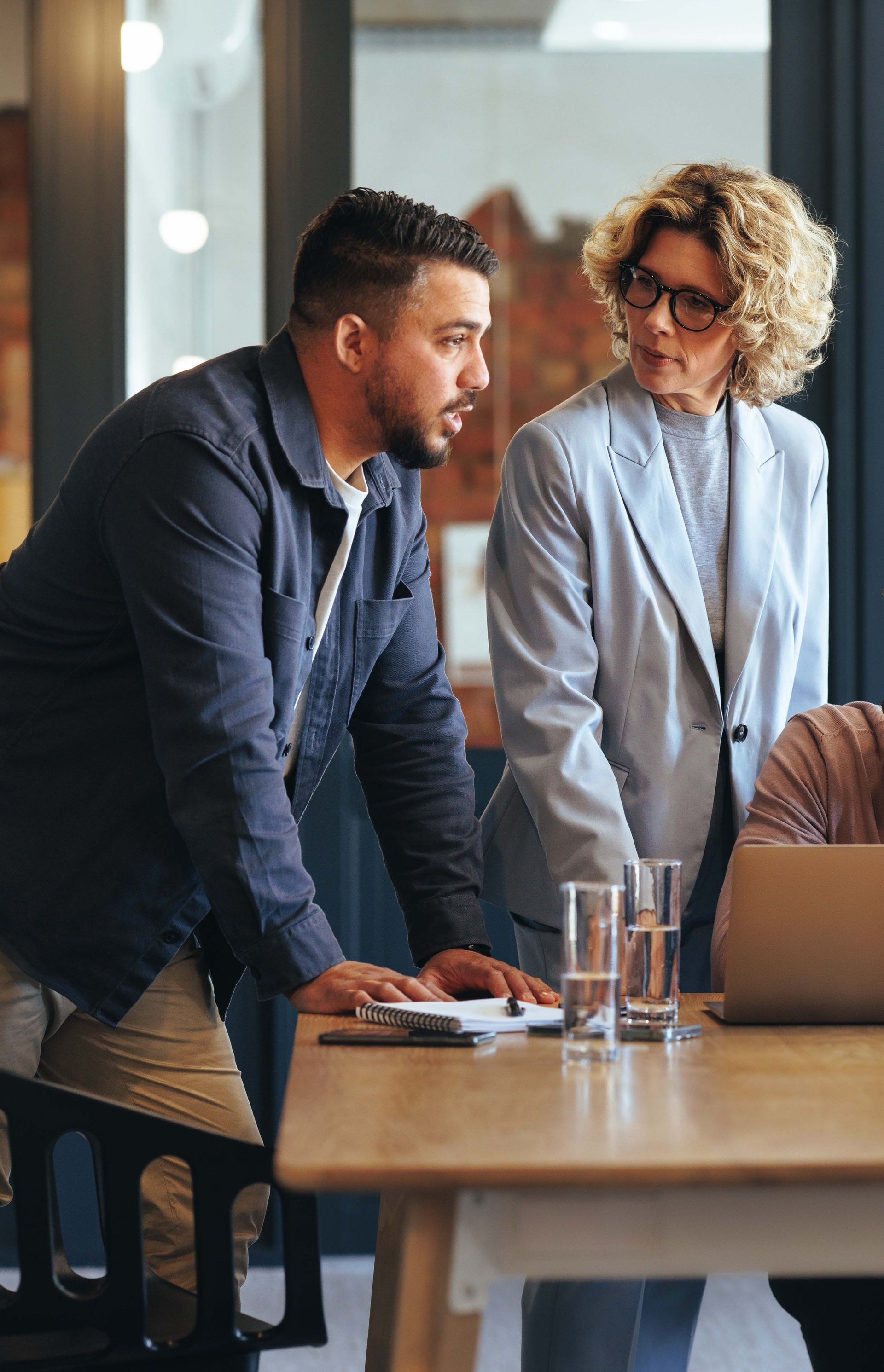 A man and a woman are standing at a table looking at a laptop.