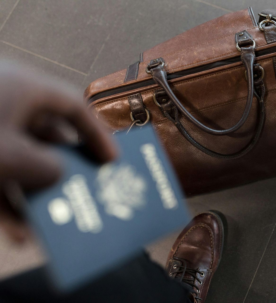 A person holding a passport next to a brown bag