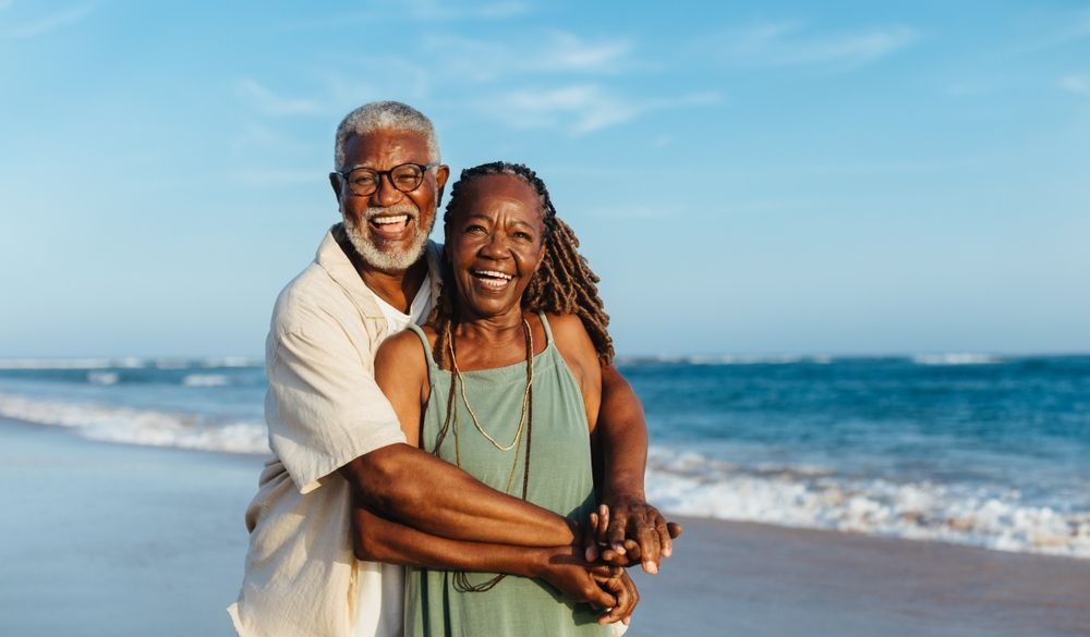 An elderly couple is hugging each other on the beach.