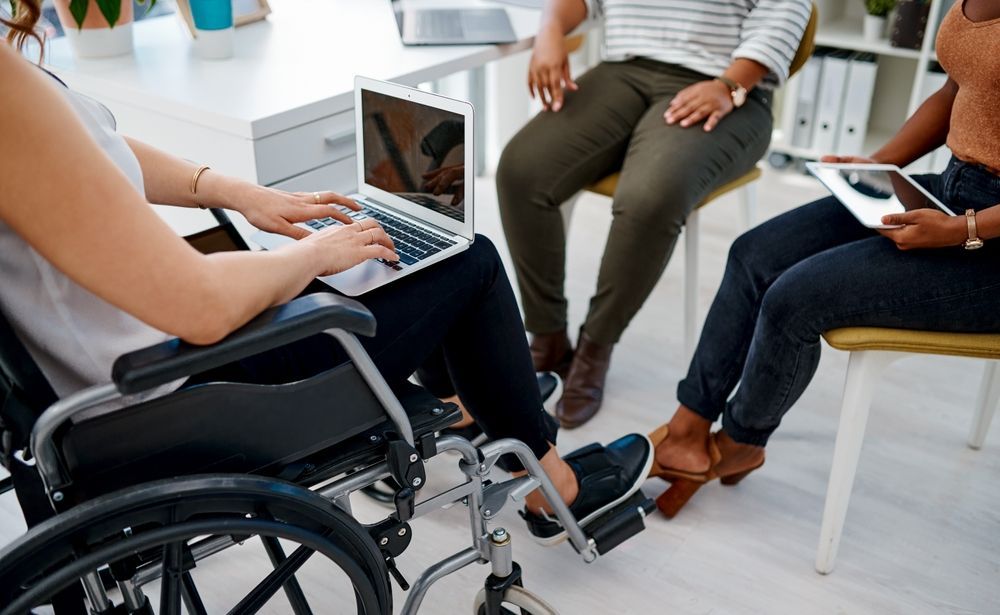 A woman in a wheelchair is using a laptop computer while sitting in a circle with other people.