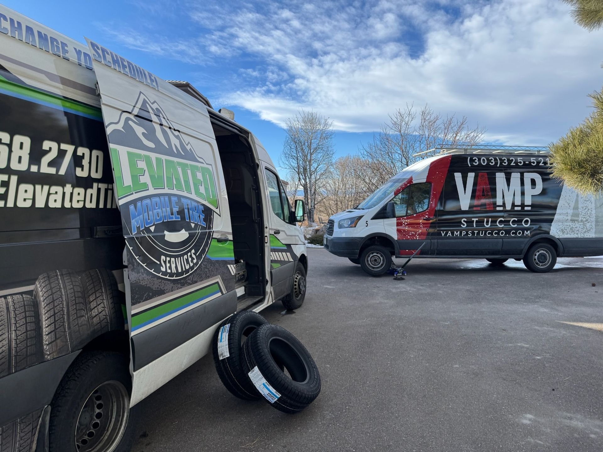 Two vans with open doors, one with tires on the ground. Outdoor setting with cloudy sky.