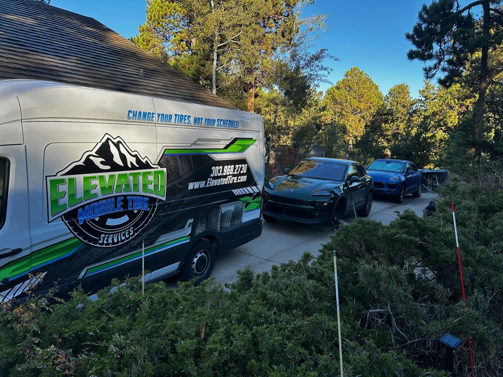 A van, Dodge Challenger, and truck parked in front of a house, business logo on the van.