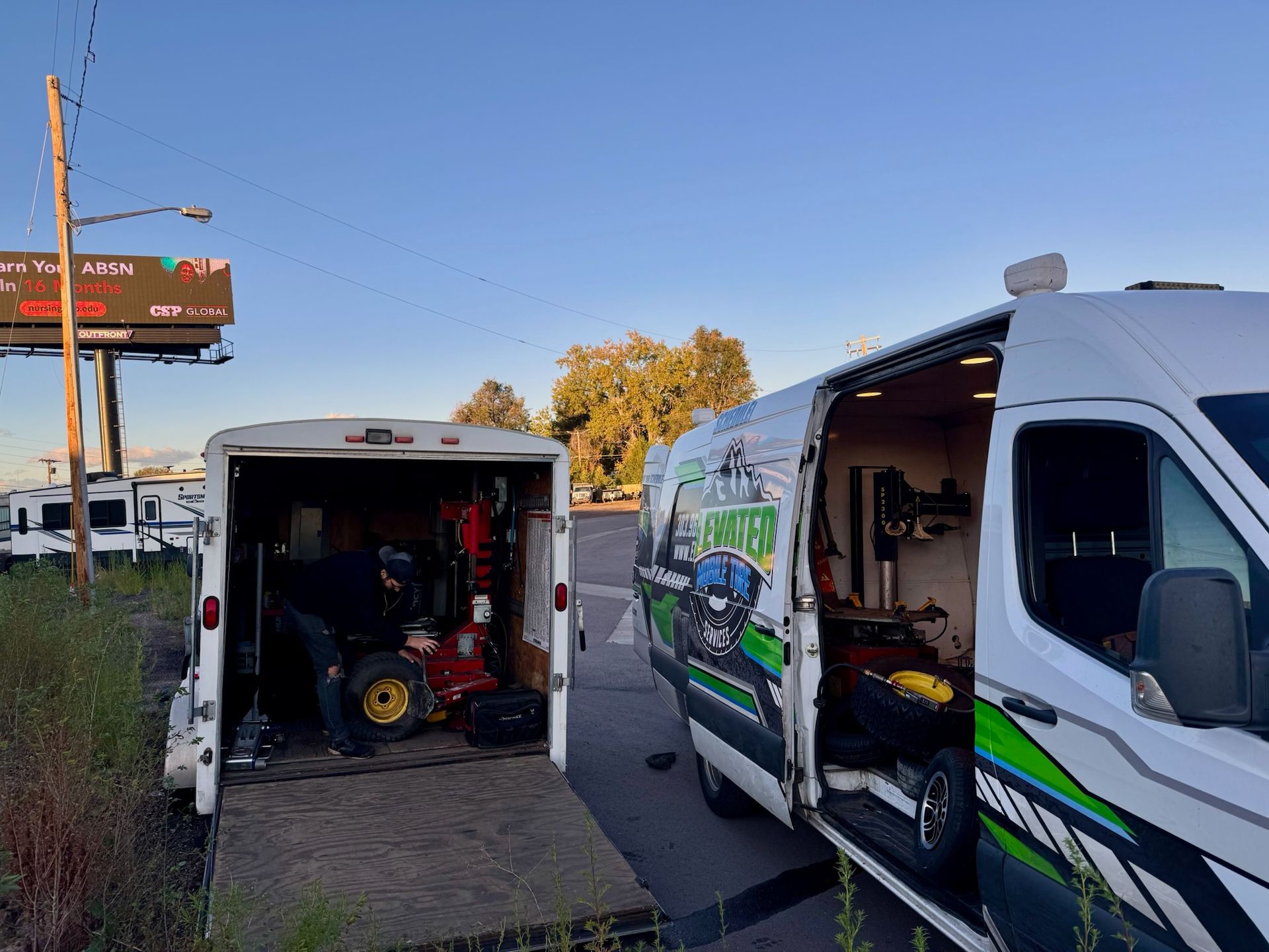 White van and trailer, open, parked on a roadside. Lawn equipment visible inside.