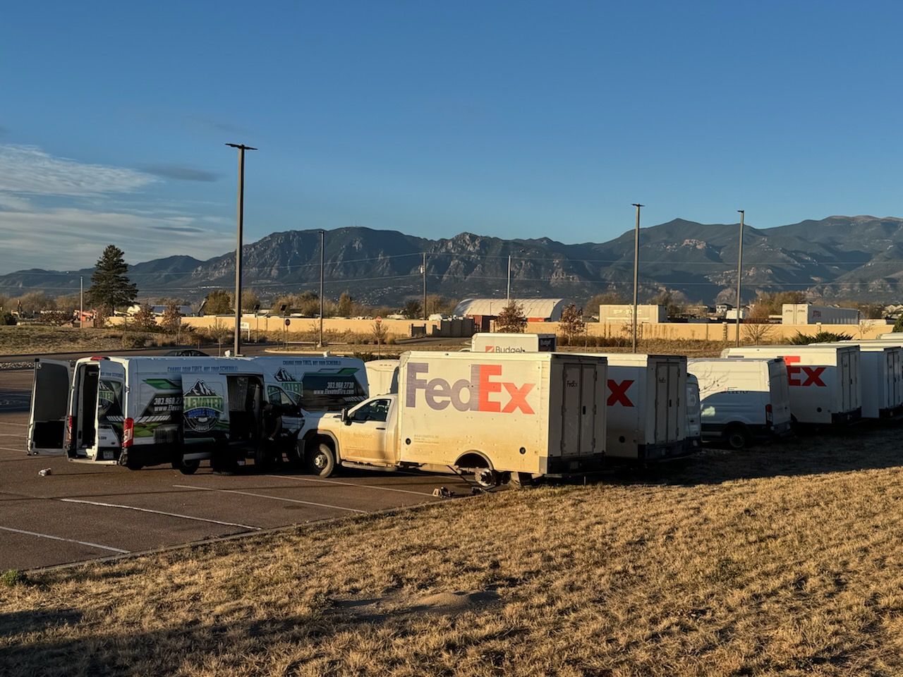 FedEx and other delivery trucks parked in a lot; mountains and blue sky in the background.