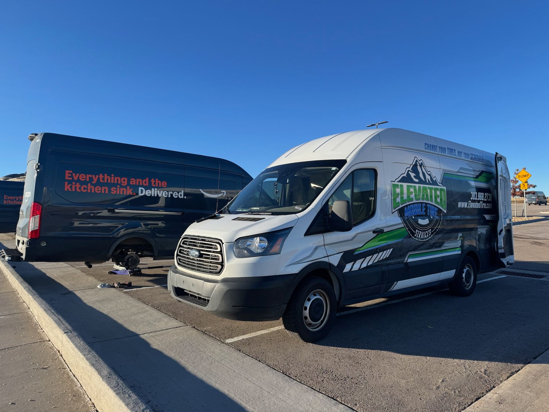 Two white and black vans parked outside on a sunny day. One van has its door open, advertising 